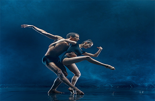 Young couple of ballet dancers dancing under water splash and drops. Young caucasian and afro american models. Man and woman dancing together. Ballet and contemporary choreography concept. Art photo