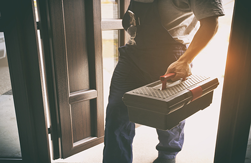 The repairer is coming in the house with toolbox in his hand